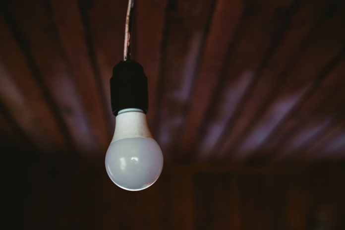 A close-up shot of a single light bulb hanging from a wooden ceiling.