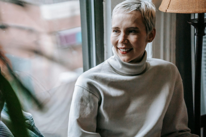 A smiling woman relaxing near a window.